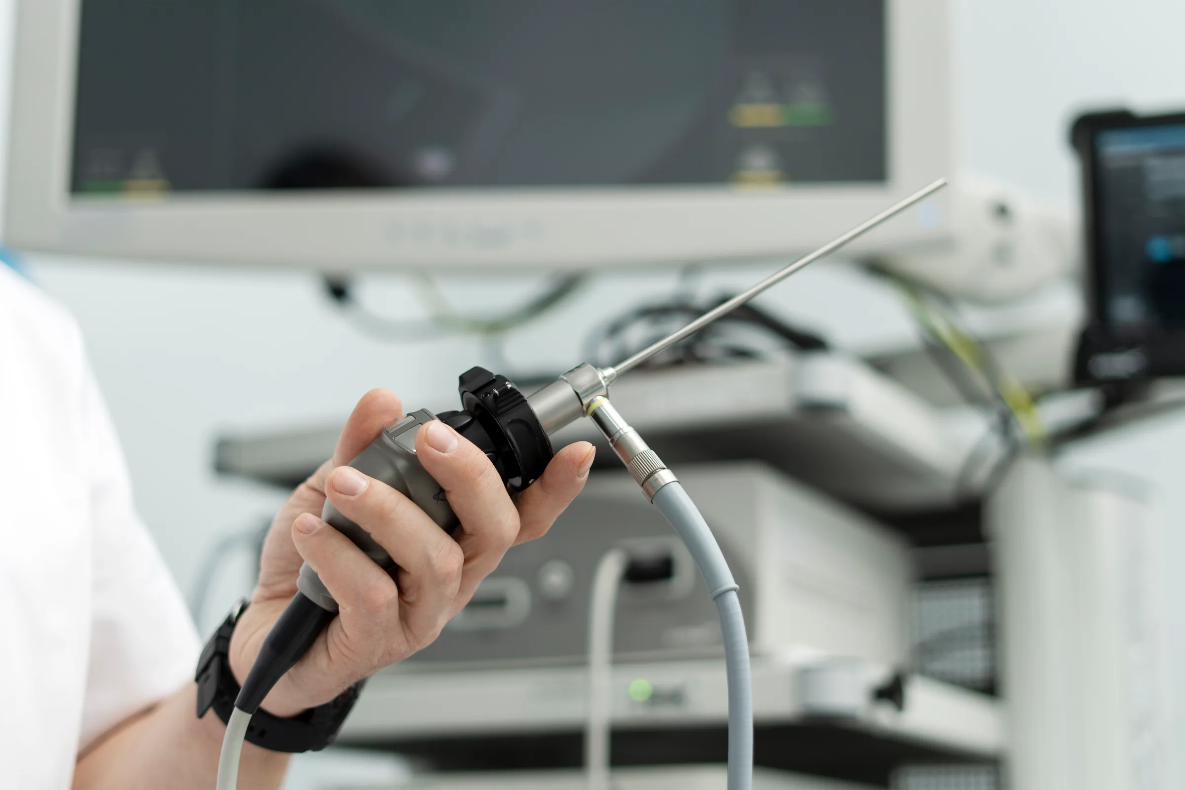 Gloved hand holding a rigid endoscope in front of a monitor