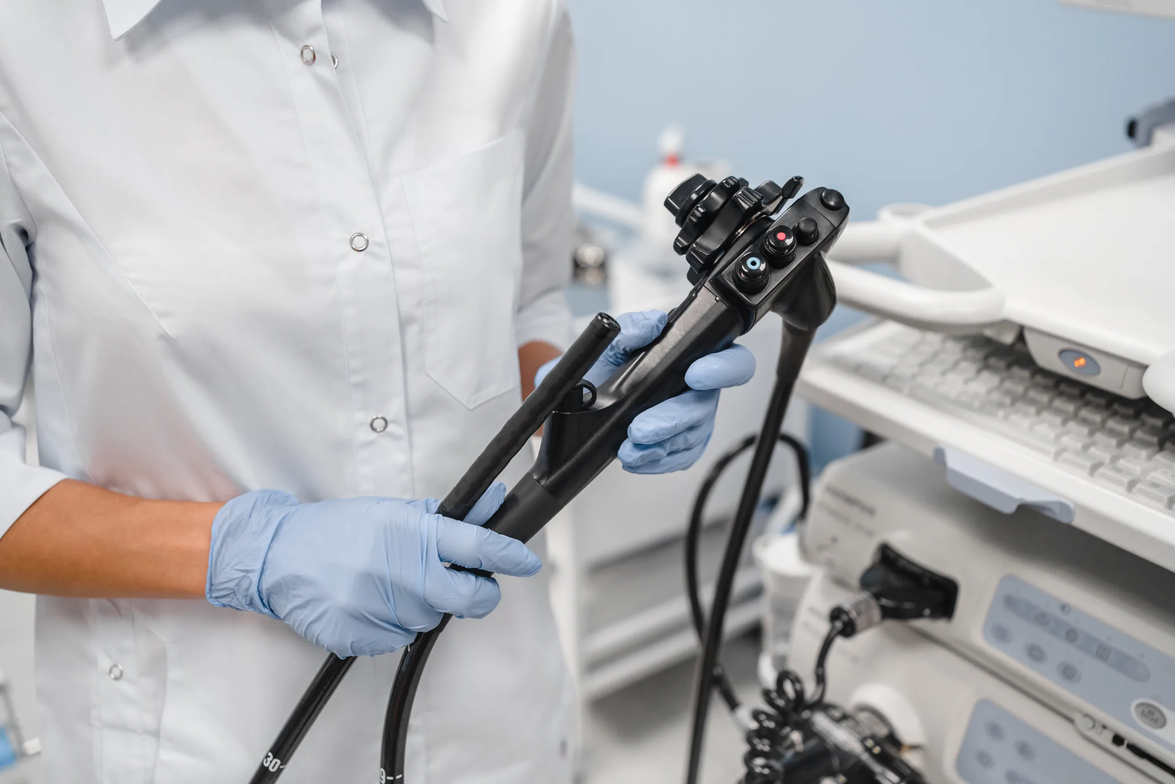 Gloved clinician inspecting a flexible endoscope beside a processing tower