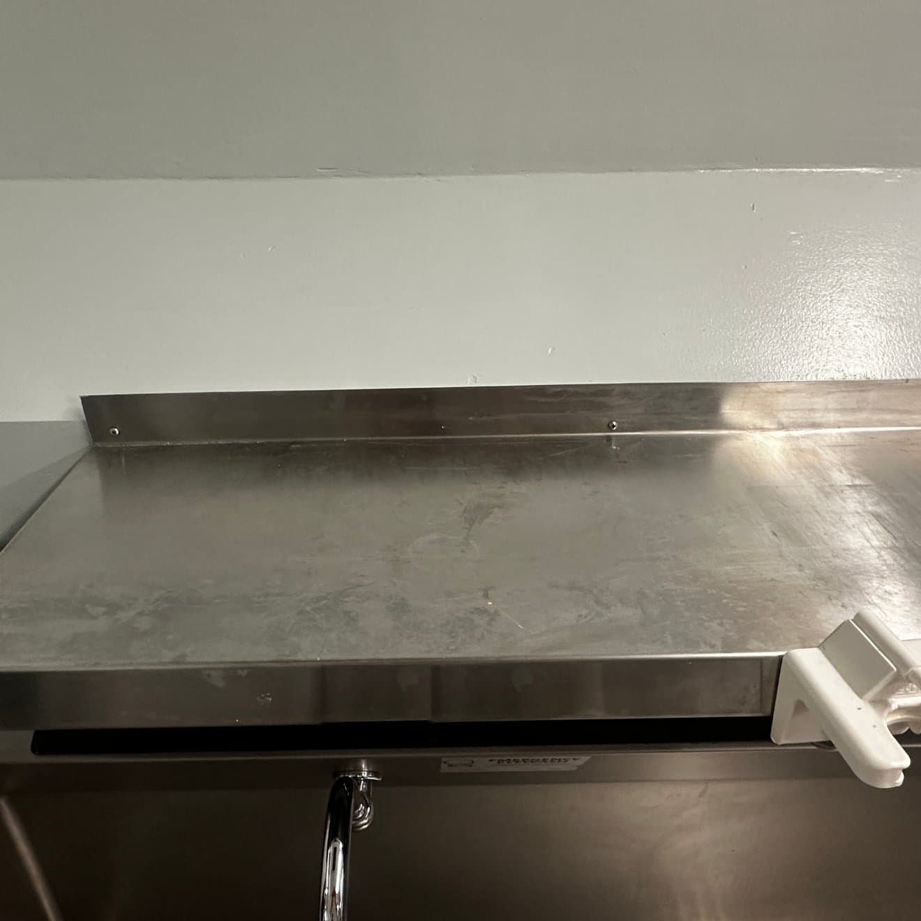 A cloudy, water-spotted stainless steel work surface and backsplash before deep cleaning by Maximo Medical