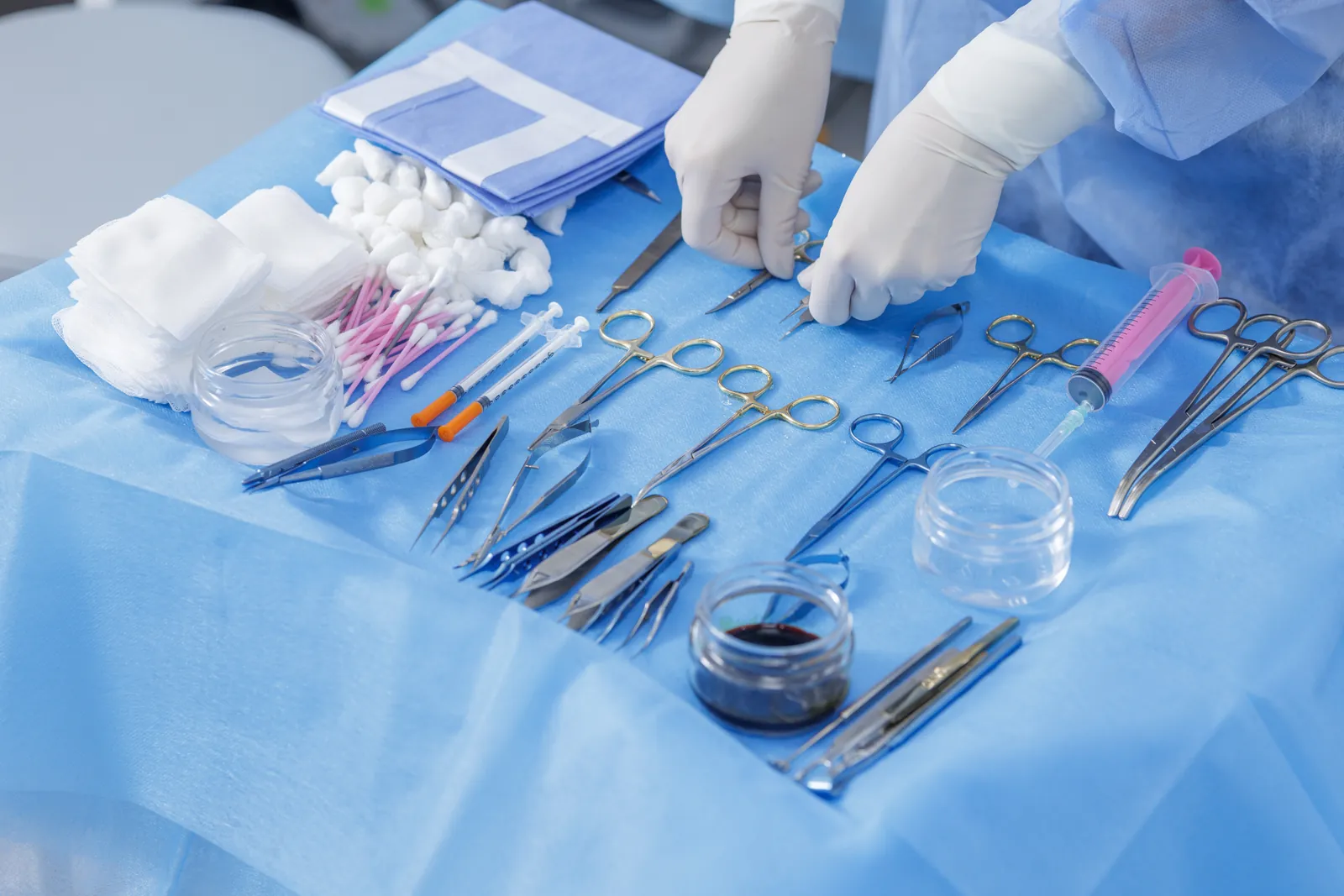 Gloved hands arranging surgical instruments laid out on a sterile blue drape